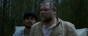 Movie still from “In Dubious Battle” (2016), directed by James Franco – A man with a beard is standing next to another man; Medium shot, Low angle