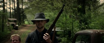 Movie still from “In Dubious Battle” (2016), directed by James Franco – A man in a fedora holding a rifle; Medium shot, Low angle