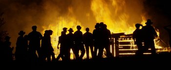 Movie still from “In Dubious Battle” (2016), directed by James Franco – A group of people standing in front of a burning building; Wide shot, Low angle
