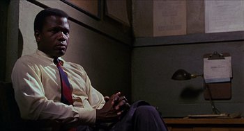 Movie still from “In the Heat of the Night” (1967), directed by Norman Jewison – A man sitting in front of a lamp in a dimly - lit room; Medium shot, Low angle