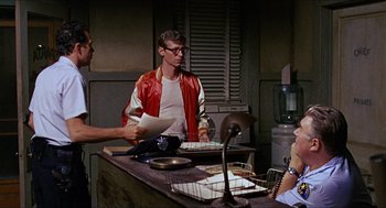 Movie still from “In the Heat of the Night” (1967), directed by Norman Jewison – A group of people standing around a table; Medium shot, Over the shoulder angle