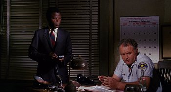 Movie still from “In the Heat of the Night” (1967), directed by Norman Jewison – Two men are sitting at a table and one of them is holding a cell phone; Medium shot, Low angle