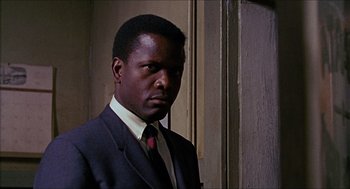 Movie still from “In the Heat of the Night” (1967), directed by Norman Jewison – A man wearing a suit and tie standing in front of a wall; Close Up shot, Low angle