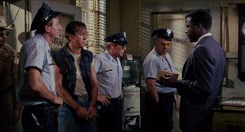 Movie still from “In the Heat of the Night” (1967), directed by Norman Jewison – A group of men standing next to each other in a room; Medium shot, Over the shoulder angle