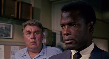 Movie still from “In the Heat of the Night” (1967), directed by Norman Jewison – A man in a suit and tie standing next to another man in a suit and tie; Close Up shot, Over the shoulder angle