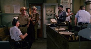 Movie still from “In the Heat of the Night” (1967), directed by Norman Jewison – A group of people standing around a room; Wide shot, Over the shoulder angle