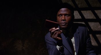 Movie still from “In the Heat of the Night” (1967), directed by Norman Jewison – A man in a suit and tie holding a wallet; Close Up shot, Over the shoulder angle