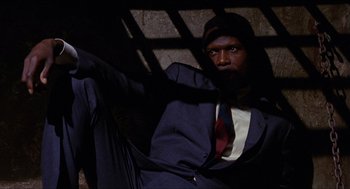 Movie still from “In the Heat of the Night” (1967), directed by Norman Jewison – A man in a suit and tie leaning against a wall; Medium shot, High angle