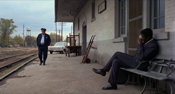 Movie still from “In the Heat of the Night” (1967), directed by Norman Jewison – A man sitting on a bench on the side of the street; Wide shot, Over the shoulder angle