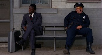 Movie still from “In the Heat of the Night” (1967), directed by Norman Jewison – Two police officers sitting on a wooden bench; Wide shot, Over the shoulder angle