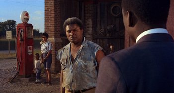 Movie still from “In the Heat of the Night” (1967), directed by Norman Jewison – A man with a beard is standing in front of two other men; Medium shot, Over the shoulder angle