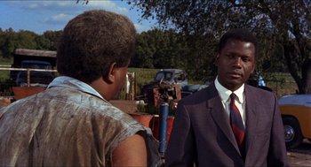 Movie still from “In the Heat of the Night” (1967), directed by Norman Jewison – A man in a suit and tie talking to a woman; Medium shot, Over the shoulder angle