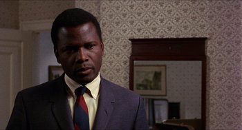 Movie still from “In the Heat of the Night” (1967), directed by Norman Jewison – A man wearing a suit and tie in a room; Close Up shot, Over the shoulder angle