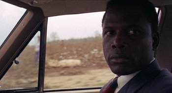 Movie still from “In the Heat of the Night” (1967), directed by Norman Jewison – A man in a suit sitting in a car looking out the window; Close Up shot, Over the shoulder angle