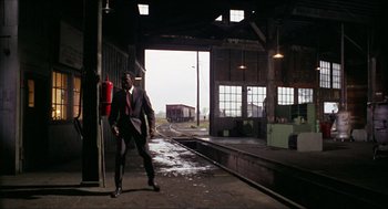 Movie still from “In the Heat of the Night” (1967), directed by Norman Jewison – A man standing in a train station next to a fire hydrant; Wide shot, Low angle