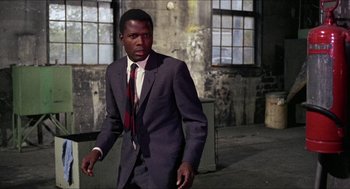 Movie still from “In the Heat of the Night” (1967), directed by Norman Jewison – A man wearing a suit and tie walking in a building; Medium shot, Low angle