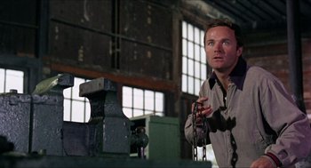 Movie still from “In the Heat of the Night” (1967), directed by Norman Jewison – A man standing next to a machine in a factory; Medium shot, Low angle