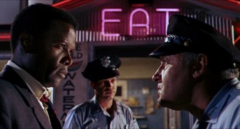 Movie still from “In the Heat of the Night” (1967), directed by Norman Jewison – A group of men standing next to each other in front of a building; Medium shot, Over the shoulder angle
