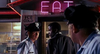 Movie still from “In the Heat of the Night” (1967), directed by Norman Jewison – A group of men standing next to each other on the street; Medium shot, Over the shoulder angle