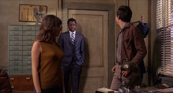 Movie still from “In the Heat of the Night” (1967), directed by Norman Jewison – A man in a suit standing next to two other men; Medium shot, Over the shoulder angle