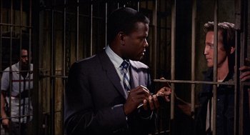 Movie still from “In the Heat of the Night” (1967), directed by Norman Jewison – A man wearing a suit and tie holding a cell phone; Medium shot, Over the shoulder angle