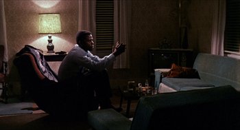 Movie still from “In the Heat of the Night” (1967), directed by Norman Jewison – A man sitting on a chair in a living room; Medium shot, Over the shoulder angle
