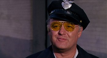 Movie still from “In the Heat of the Night” (1967), directed by Norman Jewison – A man wearing a police uniform and sunglasses; Close Up shot, Low angle