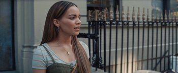 Movie still from “In the Heights” (2021), directed by Jon M. Chu – A beautiful young woman with long brown hair standing next to a fence; Close Up shot, Over the shoulder angle