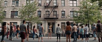Movie still from “In the Heights” (2021), directed by Jon M. Chu – A group of people standing in front of an apartment building; Extreme Wide shot, High angle