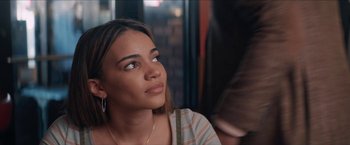 Movie still from “In the Heights” (2021), directed by Jon M. Chu – A woman sitting in front of a brick wall looking up; Close Up shot, Over the shoulder angle