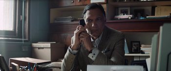 Movie still from “In the Heights” (2021), directed by Jon M. Chu – A man sitting at a desk holding a phone to his ear; Close Up shot, Low angle