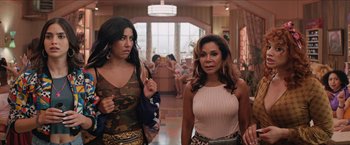 Movie still from “In the Heights” (2021), directed by Jon M. Chu – Two women are walking in a room with people in the background; Medium shot, Over the shoulder angle