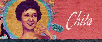 Movie still from “In the Heights” (2021), directed by Jon M. Chu – A mural of a woman with a microphone on the side of a building; Extreme Close Up shot, Low angle