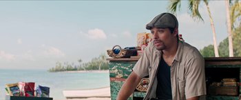 Movie still from “In the Heights” (2021), directed by Jon M. Chu – A man sitting next to an old chest on the beach; Medium shot, Over the shoulder angle