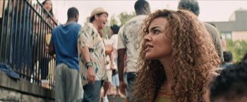 Movie still from “In the Heights” (2021), directed by Jon M. Chu – A person with curly hair near a crowd; Close Up shot, Over the shoulder angle