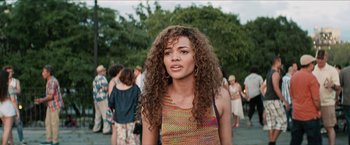 Movie still from “In the Heights” (2021), directed by Jon M. Chu – A woman with curly hair standing in front of a group of people; Close Up shot, Over the shoulder angle