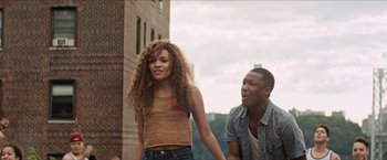 Movie still from “In the Heights” (2021), directed by Jon M. Chu – A man and a woman holding hands in front of a brick building; Medium shot, Low angle
