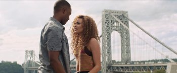 Movie still from “In the Heights” (2021), directed by Jon M. Chu – A man and a woman standing next to each other near a bridge; Medium shot, Over the shoulder angle