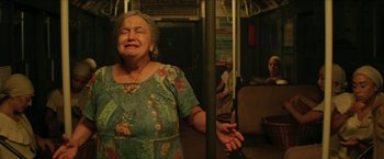 Movie still from “In the Heights” (2021), directed by Jon M. Chu – An older woman standing on a train with her eyes closed; Medium shot, Low angle