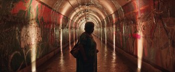 Movie still from “In the Heights” (2021), directed by Jon M. Chu – A woman standing in a tunnel with a bag in her hand; Wide shot, High angle