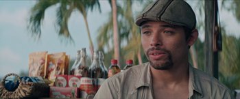 Movie still from “In the Heights” (2021), directed by Jon M. Chu – A man in a hat standing in front of bottles of alcohol; Close Up shot, Over the shoulder angle