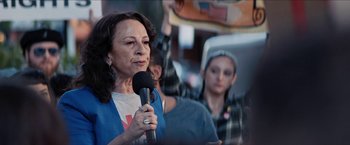 Movie still from “In the Heights” (2021), directed by Jon M. Chu – A woman is holding a microphone while a crowd of people watch; Medium shot, Low angle