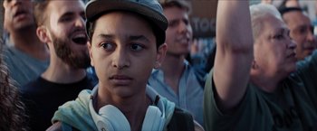 Movie still from “In the Heights” (2021), directed by Jon M. Chu – A young boy wearing a hat and headphones is looking at the camera; Close Up shot, Over the shoulder angle