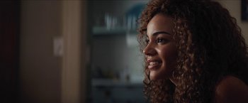 Movie still from “In the Heights” (2021), directed by Jon M. Chu – A person with curly hair smiling; Close Up shot, Over the shoulder angle