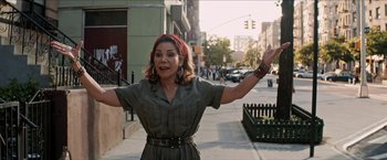 Movie still from “In the Heights” (2021), directed by Jon M. Chu – A woman standing on the side of the street with her arms outstretched; Medium shot, Over the shoulder angle