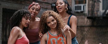 Movie still from “In the Heights” (2021), directed by Jon M. Chu – A group of young women standing next to each other on a street; Medium shot, Over the shoulder angle