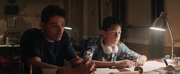 Movie still from “In the Heights” (2021), directed by Jon M. Chu – Two young men sitting at a table in front of a laptop computer; Medium shot, Over the shoulder angle