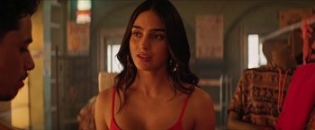 Movie still from “In the Heights” (2021), directed by Jon M. Chu – A woman in a red top is standing in a room; Close Up shot, Over the shoulder angle