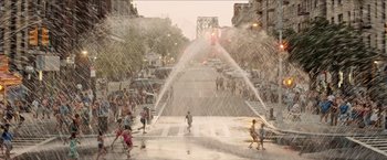 Movie still from “In the Heights” (2021), directed by Jon M. Chu – A group of people standing in the rain near a fire hydrant; Extreme Wide shot, High angle