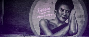 Movie still from “In the Heights” (2021), directed by Jon M. Chu – A mural on a brick wall of a woman with long black hair; Wide shot, Low angle